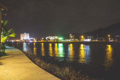 Illuminated city by river against sky at night