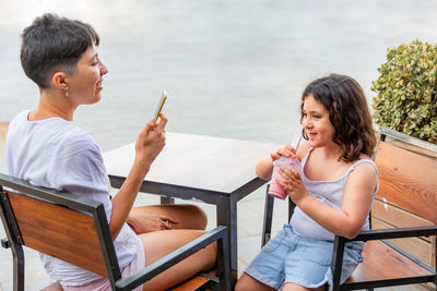 Mother and daughter drinking milkshake and using the mobile phone