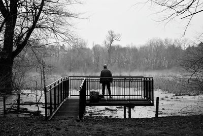 Rear view of man standing on observation point over lake against sky in forest