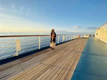 Woman standing on railing by sea against sky