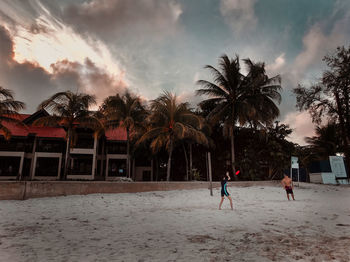 People playing soccer on beach against sky during sunset