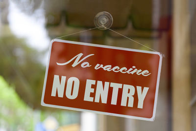 Close-up on a red sign in the window of a shop displaying the message no vaccine, no entry .
