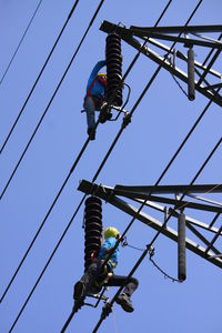 Low angle view of workers on built structure against clear blue sky