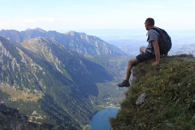 Full length of hiker sitting on cliff while looking at tatra mountains