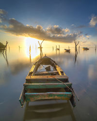 Wooden posts in lake against sky during sunset