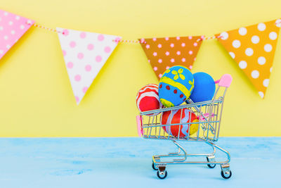 Easter eggs in toy shopping cart on table against bunting