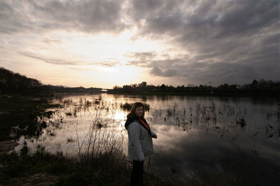 Woman standing on lake against sky during sunset