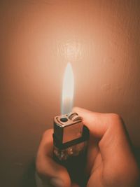 Close-up of hand holding burning candle against wall