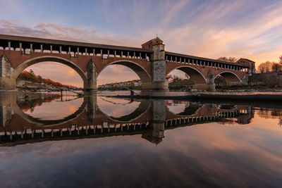 Arch bridge over river against sky during sunset