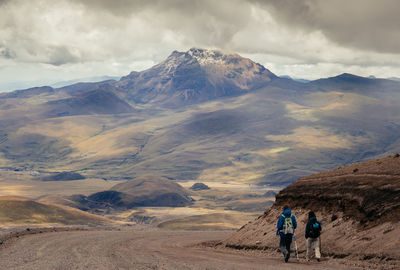 Rear view of men walking on mountain against sky