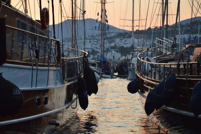 Sailboats moored in harbor at sunset