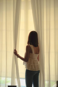 Rear view of woman looking through window at home