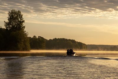 Rear view of man in boat on lake against sky during sunset