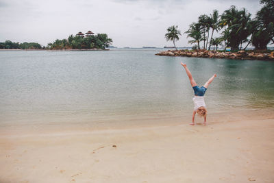 Full length of young woman performing handstand at seashore