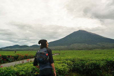 Rear view of man standing on field against mountain and sky