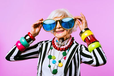 Portrait of senior woman wearing sunglasses against colored background