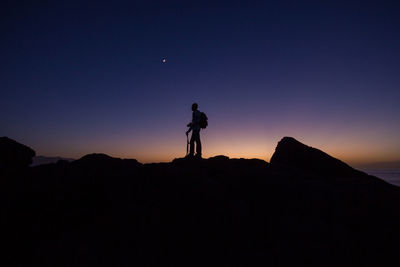 Silhouette man standing on rock against sky during sunset