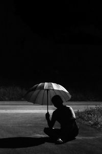 Rear view of man holding umbrella sitting at beach 