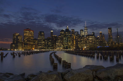 Illuminated buildings by river against sky at night