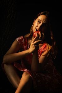 Woman looking away while sitting against black background