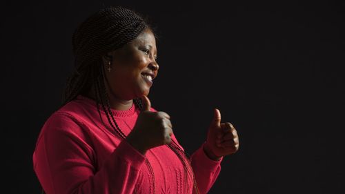 Portrait of young woman standing against black background