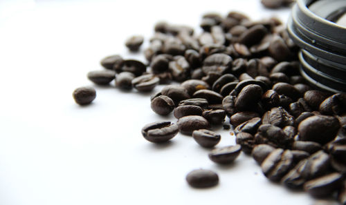 Close-up of lens on roasted coffee beans against white background