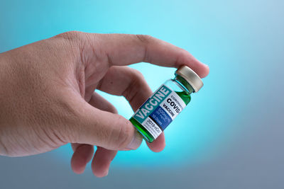 Close-up of hand holding bottle against blue background