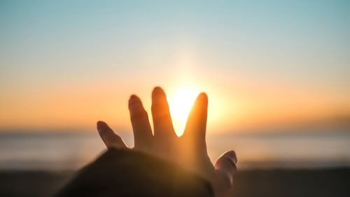 Hand against sky during sunset