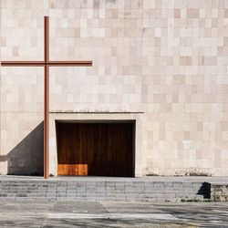 Religious cross on footpath against wall of building