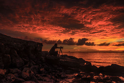 Silhouette rock on beach against sky during sunset