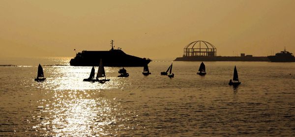 Silhouette fishing boats in sea against orange sky