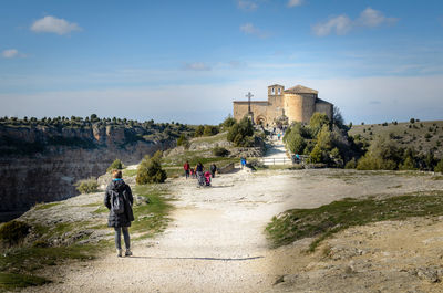 Rear view of woman with backpack waking on footpath towards church against sky