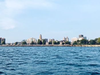 Sea by buildings in city against sky