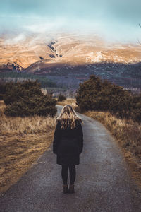 Rear view of woman standing on road against mountains