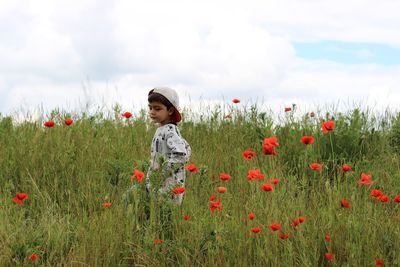 Boy walking on poppy field against sky