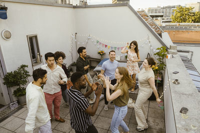 Group of carefree male and female friends dancing while celebrating during dinner party in balcony