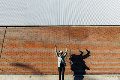 Businesswoman wearing virtual reality with arms raised in front of wall