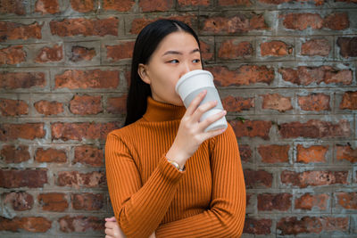 Portrait of man holding coffee cup against brick wall