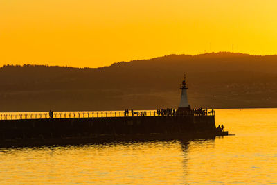 Silhouette of lighthouse at seaside during sunset