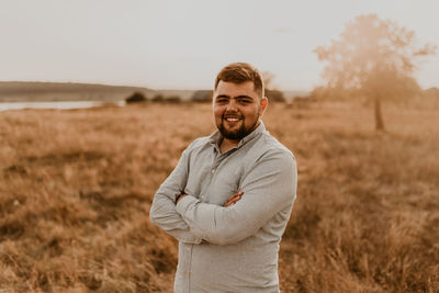 Portrait of young man standing on field against sky