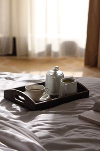 Cup with kettle in serving tray on bed at home