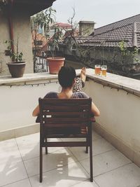 Rear view of man sitting on chair against building