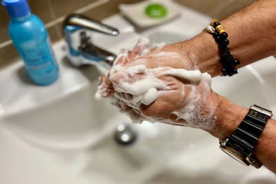 Close-up of man hand with faucet in bathroom