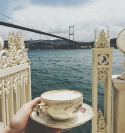 Close-up of coffee cup on table by river against sky