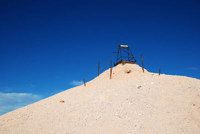 Low angle view of built structure on sand against blue sky