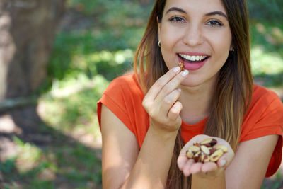 Close-up of healthy brazilian woman picking brazil nuts from her hand in park. looks at camera.