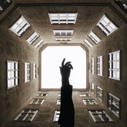 Cropped hand of person amidst buildings against clear sky