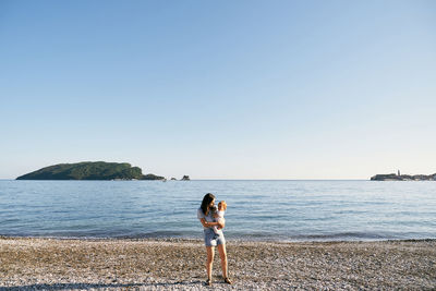 Rear view of women standing on beach against clear sky