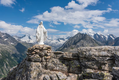 White statue of virgin mary, mother of god, placed on top of the mountains, blue sky, white clouds.