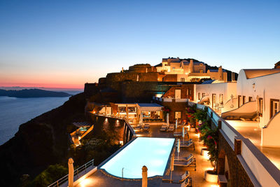 Buildings by swimming pool in city against sky during sunset